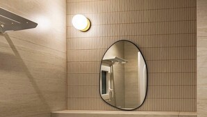 Ein modernes Badezimmer mit einem beigen Waschbecken, einem runden Spiegel und einer Wandleuchte.
