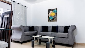 Un salón con un sofá gris, una mesa de centro de cristal y un cuadro abstracto colgado en la pared.