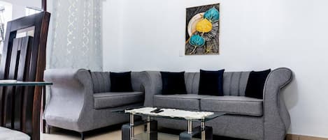 A living room with a grey sofa, a glass coffee table, and a wall-mounted abstract painting.