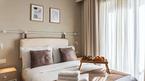 A neatly made bed with pillows, a tray of fruits, and towels on a bedside table in a hotel room. - Travi Boutique By Holi 18 (Saint Julian's)