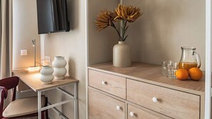 A modern room with a flat-screen TV mounted on the wall, a wooden desk with a vase of flowers, and a glass pitcher with oranges on a wooden cabinet. - Travi Boutique By Holi 18 (Saint Julian's)