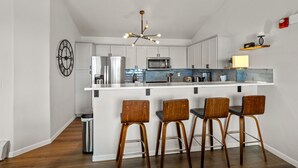 Una cocina moderna con una isla blanca, electrodomésticos de acero inoxidable y taburetes de bar de madera.