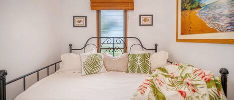 A bedroom with a bed, a window with a view, and a painting on the wall.