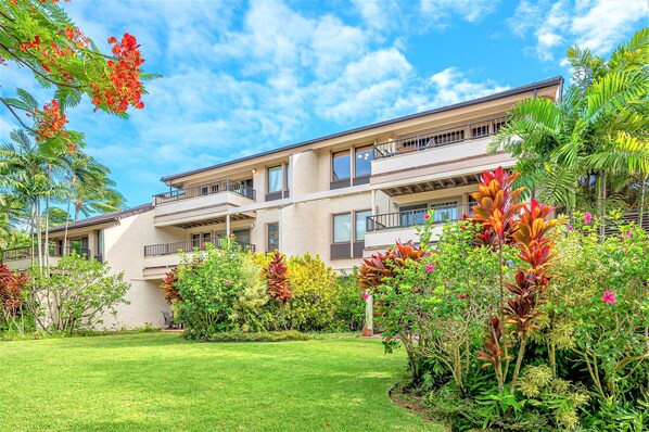 Un immeuble à plusieurs étages doté de balcons, entouré d’une végétation luxuriante et de plantes tropicales.
