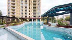 Una piscina con bordes azulejados, una zona cubierta y un edificio alto al fondo.