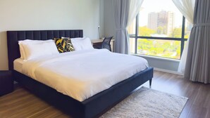 Un dormitorio moderno con una cama grande, una mesita de noche y vistas de la ciudad a través de una ventana con cortinas.