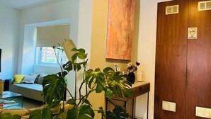 A room with a bed, a desk, and a large window. There is a plant on the desk and a painting on the wall. - 8Villa (St. Julian's)