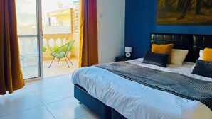 A bedroom with a bed, a nightstand, a painting, and a balcony with a chair. - 8Villa (St. Julian's)