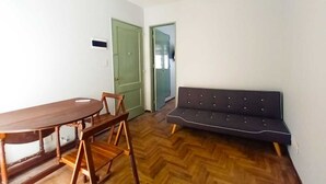 Une pièce comprenant une table à manger en bois, des chaises, un canapé foncé et un parquet à motifs en chevrons.