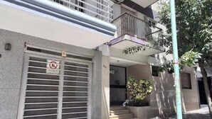Un bâtiment avec un volet fermé, un balcon et un escalier menant à l’entrée.