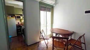 Une pièce avec une table et des chaises en bois, un coin cuisine visible à travers une porte ouverte, et un appareil de climatisation fixé au mur.