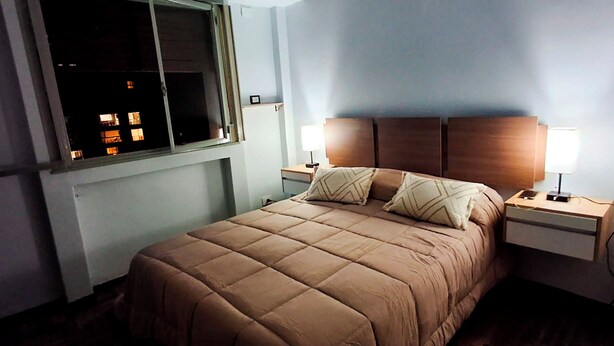 Une chambre à coucher comprenant un lit, des tables de chevet, une fenêtre et une tête de lit fixée au mur.