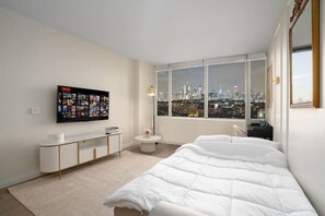Une chambre moderne avec vue sur la ville, un grand lit, un téléviseur fixé au mur et une petite table de chevet.