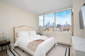 Une chambre d’hôtel avec un grand lit, une table de chevet, une lampe et une vue sur les toits de la ville, visible à travers une grande fenêtre.