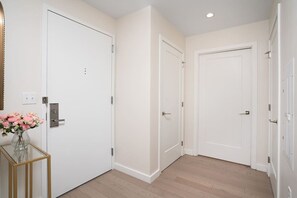 A hallway with three white doors, a glass table with a vase of flowers, and a light switch on the wall.