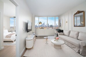 Un salon moderne avec vue sur la ville, comprenant un canapé, une table basse, un téléviseur et une petite table d’appoint.