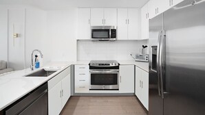 Een moderne keuken met witte kasten, een roestvrijstalen koelkast, een magnetron, een oven en een broodrooster.
