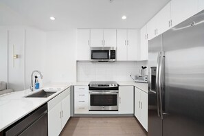 Une cuisine moderne avec des meubles blancs, un réfrigérateur en acier inoxydable, un four à micro-ondes, un four traditionnel et un grille-pain.