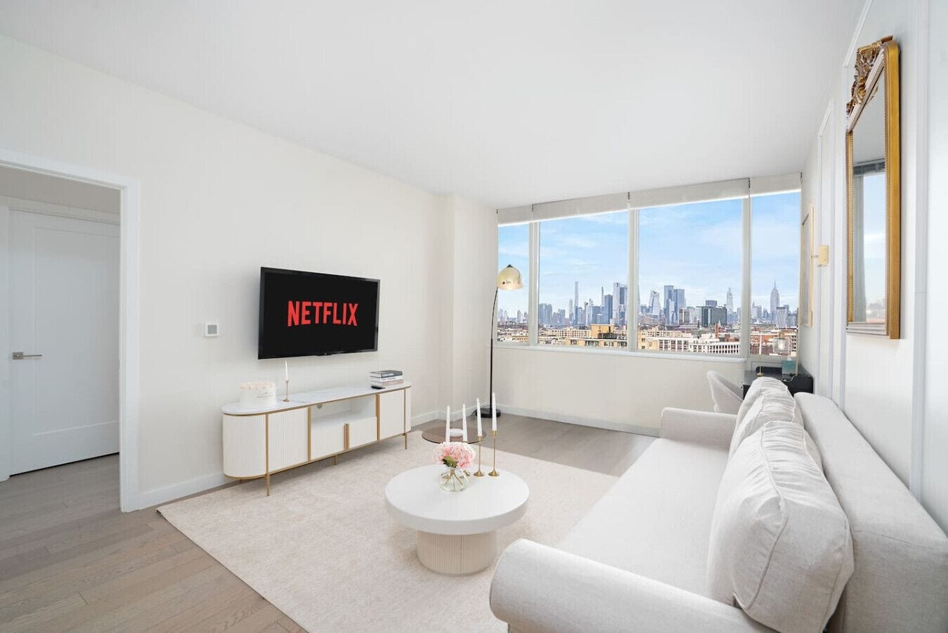 A modern living room with a large window, a white sofa, a coffee table, and a TV displaying 'NETFLIX'.