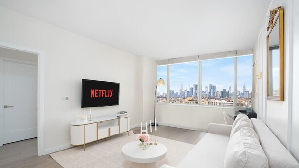Een moderne woonkamer met een groot raam, een witte bank, een salontafel en een televisie waarop 'NETFLIX' wordt weergegeven.
