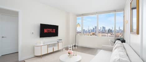 A modern living room with a large window, a white sofa, a coffee table, and a TV displaying 'NETFLIX'.