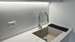 A modern kitchen with a sleek white countertop, a stainless steel sink, and a black faucet.