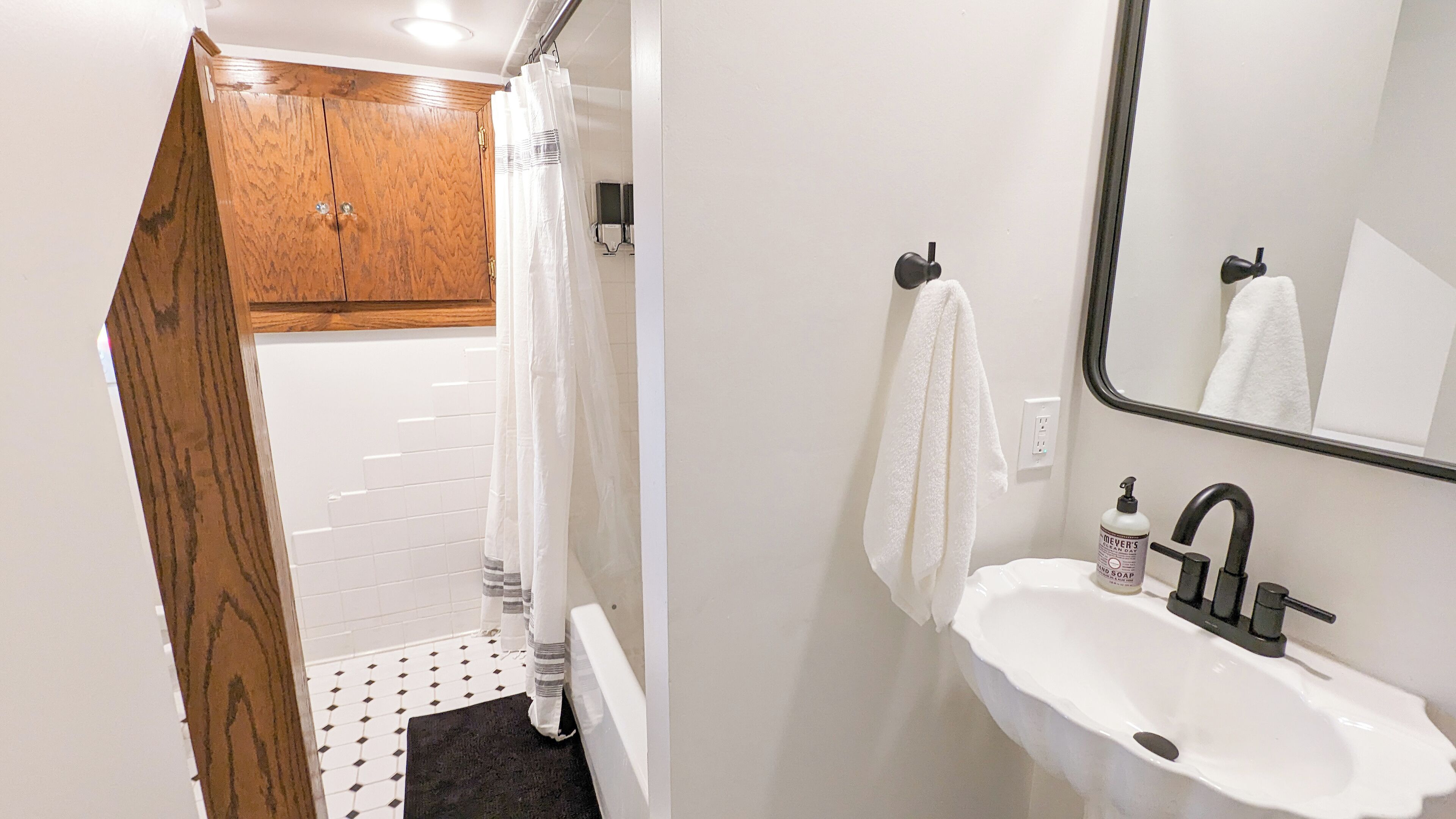 A bathroom with a white sink, a mirror, a shower curtain, and a wooden door.