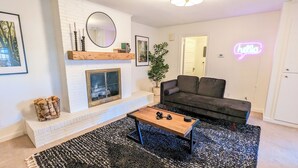 A living room with a fireplace, a black sofa, a coffee table, and a neon 'Hello' sign. - 1 bedroom apt, Steps from Swamp Rabbit Trail, 15 minute walk to Main st. (Greenville)