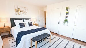 A neatly arranged bedroom with a bed, bedside tables, a bench, and a door with a plant hanging on it. - 1 bedroom apt, Steps from Swamp Rabbit Trail, 15 minute walk to Main st. (Greenville)