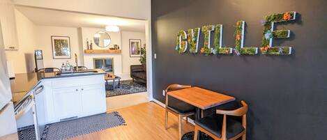 A modern kitchen with white cabinets, a wooden dining table, and a black wall with a 'BILLE' sign.