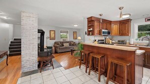 Eine moderne Küche mit Holzausbau, einer zentralen Kochinsel mit Hockern, einer eingebauten Mikrowelle und einem großen Fenster.