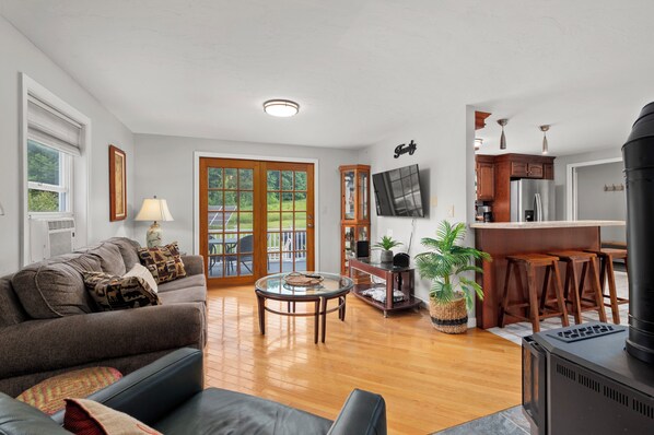 A spacious living room with a sofa, a coffee table, and a TV. There is a kitchen area with a refrigerator and a stove.