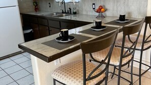 Cocina compacta con armarios oscuros, un refrigerador blanco y un pequeño comedor con una mesa y cuatro sillas.