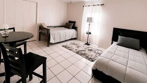 Un dormitorio con cama, escritorio, silla, ventilador de techo y ventana con cortinas.