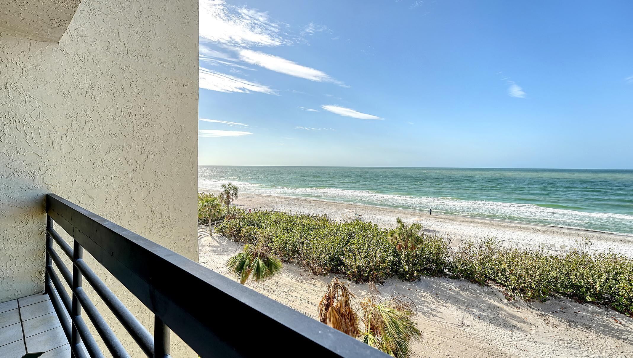 A balcony with a view of a sandy beach and the ocean.