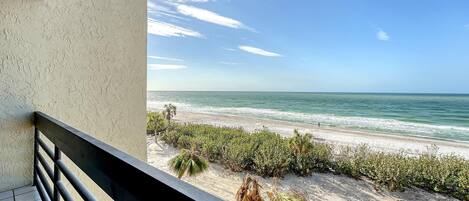 A balcony with a view of a sandy beach and the ocean.