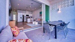 Una sala moderna con un sofá, una mesa de comedor con sillas y una cocina al fondo.