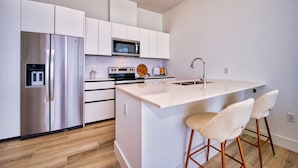Una cocina moderna con armarios blancos, electrodomésticos de acero inoxidable, una isla central con taburetes y un microondas sobre el horno.