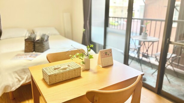 A hotel room with a bed, a wooden table with a basket and a vase, and a calendar. - Cozy Apt. In The Heart of Beppu.『Nemuri no yu』202 (Beppu)