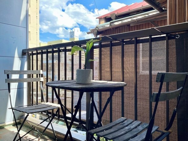 A balcony with a round table and two chairs, a potted plant, and a metal fence.