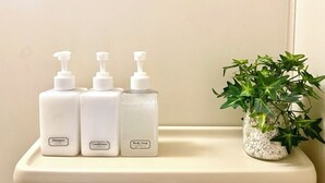 A bathroom shelf with three bottles of shampoo, conditioner, and body soap, and a small potted plant. - Cozy Apt. In The Heart of Beppu.『Nemuri no yu』202 (Beppu)
