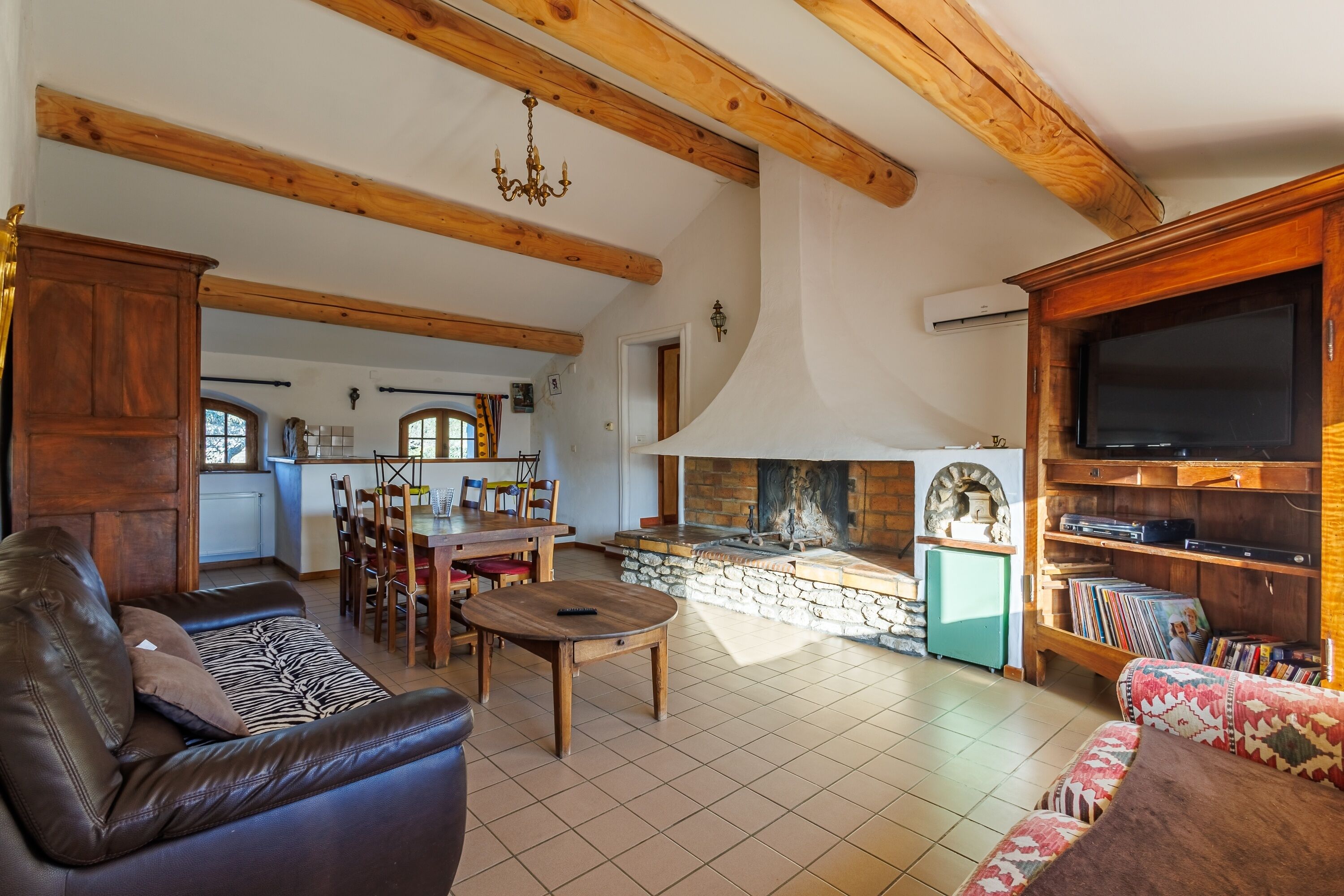 Un salón espacioso con chimenea, vigas de madera, televisor y zona de comedor.