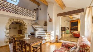 Ein gemütlicher Wohnbereich mit einem Holzesstisch, einem gemusterten Sofa und einer Treppe, die in einen oberen Bereich führt.