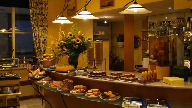 A buffet setup with various food items, a vase of flowers, and a bar area with glasses and bottles.