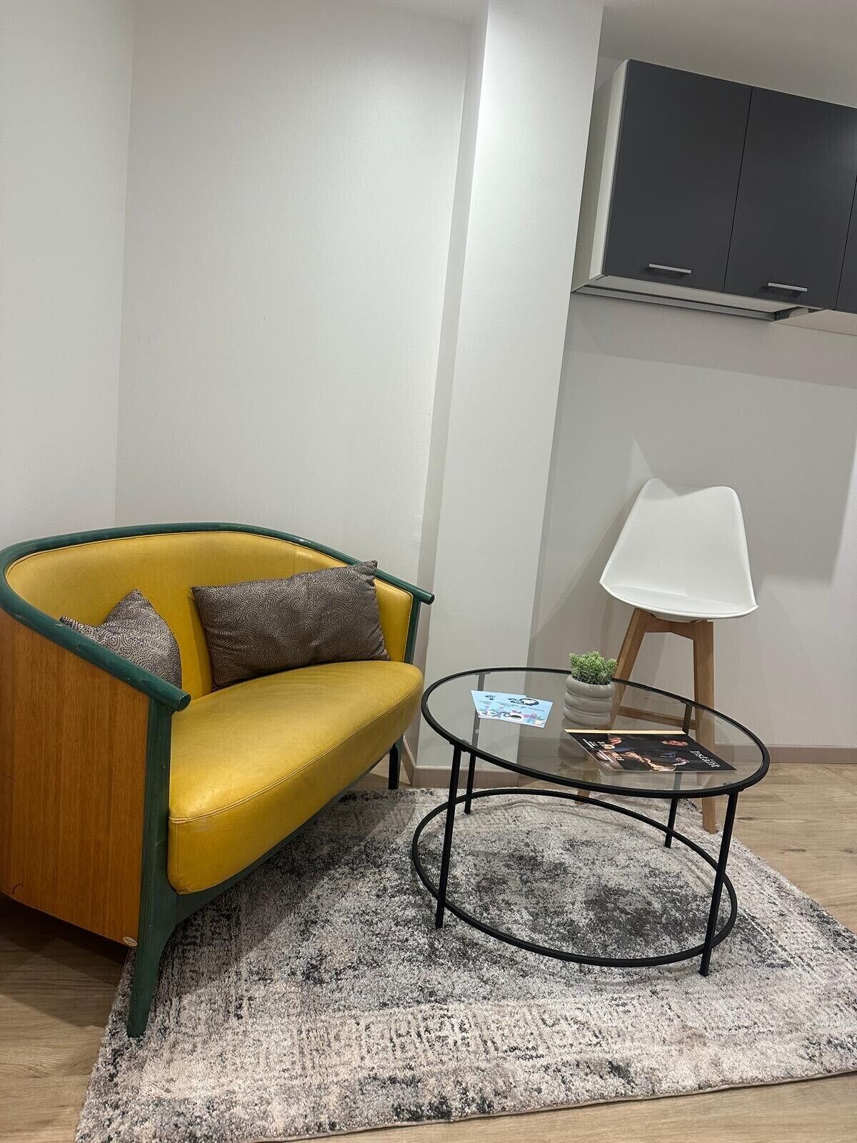 Ein gelbes Sofa mit grünen Akzenten, ein kleiner weißer Tisch und ein Blumentopf in einem modernen Wohnzimmer mit grauem Teppich.