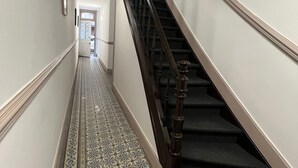 A hallway with a patterned floor leading to a staircase with a dark handrail.