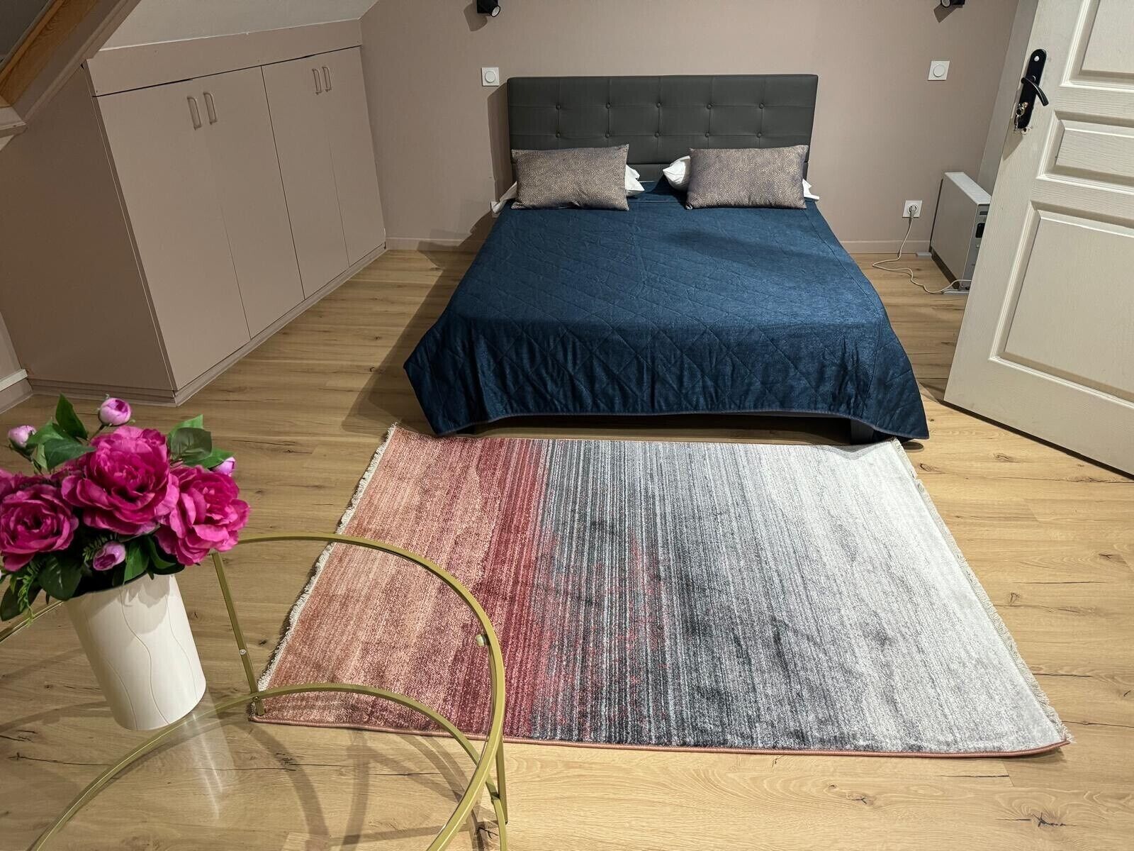 A bedroom with a bed, a bedside table, a chair, a wardrobe, and a potted plant.