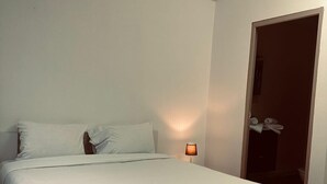 A minimalist bedroom with a single bed, a bedside lamp, and a door leading to a bathroom.