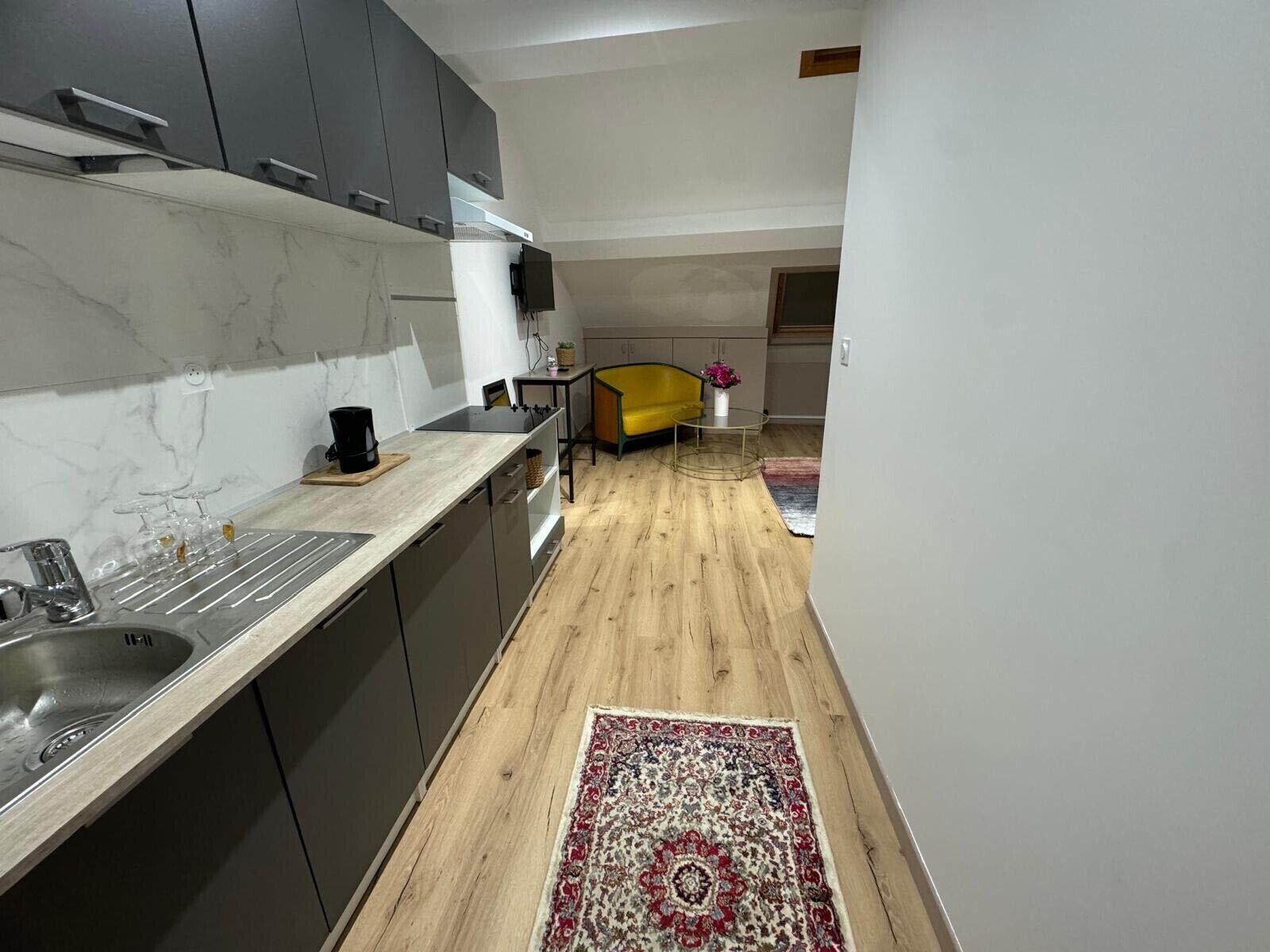 Una cocina moderna con armarios grises, un lavamanos de acero inoxidable y piso de madera.