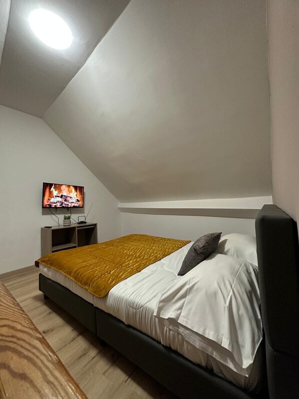A bedroom with a bed, a TV mounted on the wall, and a small nightstand. - Gîtes by Hôtel Les Reflets Jaunes (Givet)